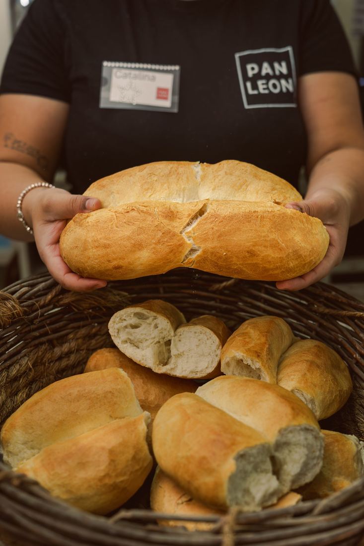Panadera de PAN LEON sosteniendo una marraqueta sobre un canasto de pan